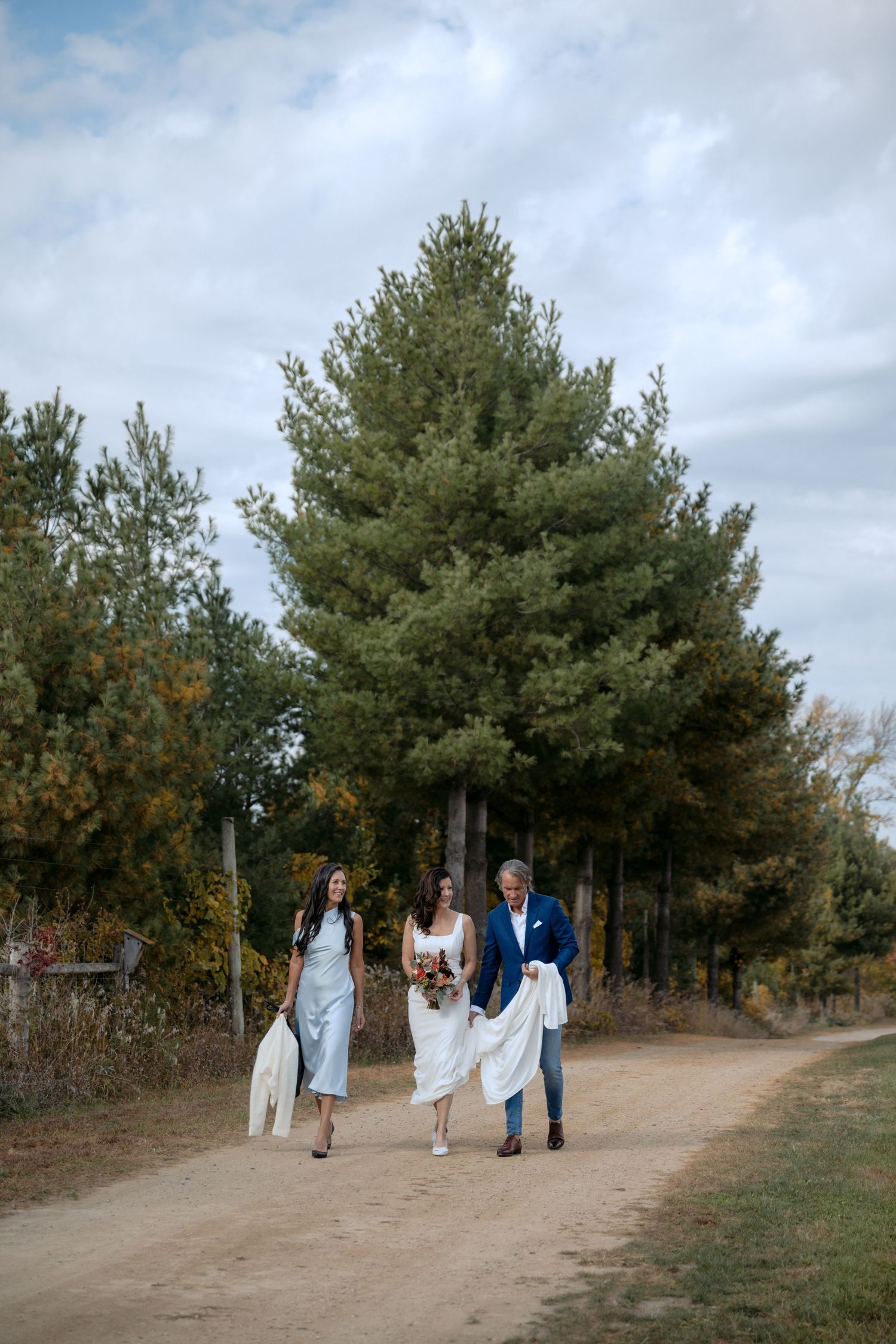 Bride walks down a treelined path to the ceremony site at Rustic Roots Winery in Scandia, MN.