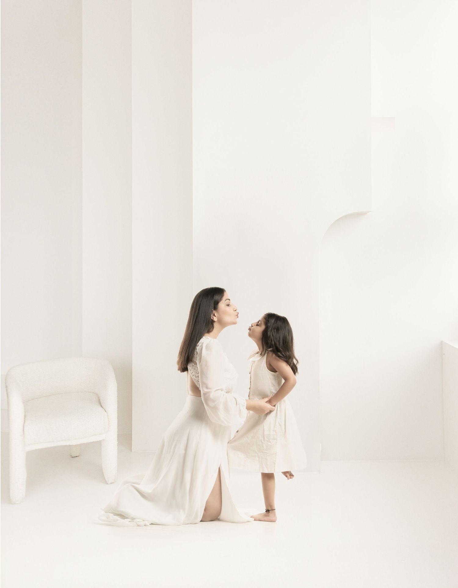 Heartwarming studio portrait of parent and child in matching white dresses against minimalist backdrop.