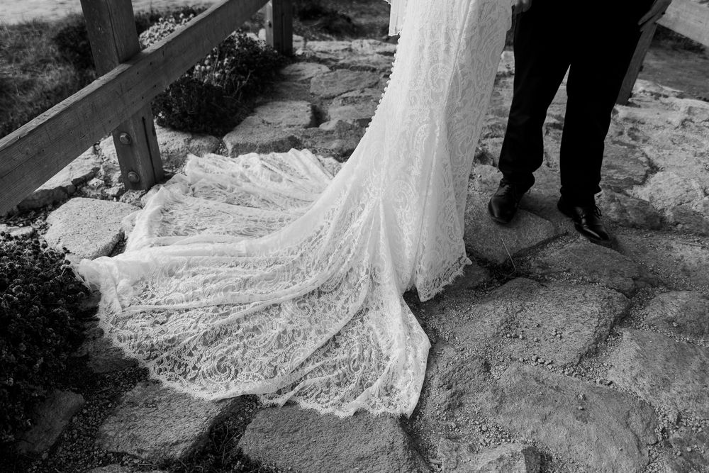 Black and white detail shot of bride's lace cathedral train spread across stone pathway.