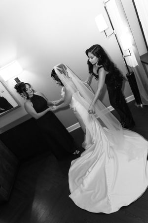Bridesmaids help a bride with her veil and wedding dress in a black and white getting ready photo.