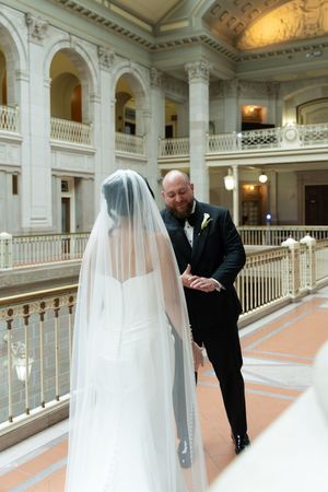 Groom in black tuxedo sees bride for first time in stunning neoclassical wedding venue first look.