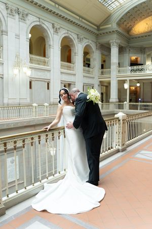Bride and groom share a romantic moment on an elegant balcony in a grand white marble wedding venue.
