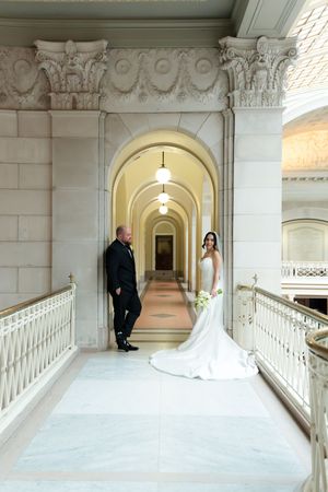 Bride and groom pose in elegant marble hallway with arched ceilings at a grand wedding venue.