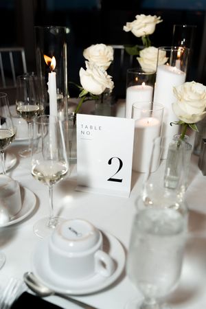 Elegant wedding reception table with white roses, pillar candles, and table number 2 card.