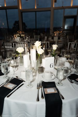 Wedding reception table 6 with white rose centerpieces, pillar candles, and black linen napkins.