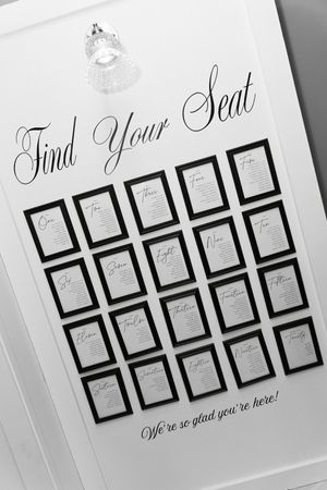 Elegant black and white wedding seating chart display with framed table numbers on white board.