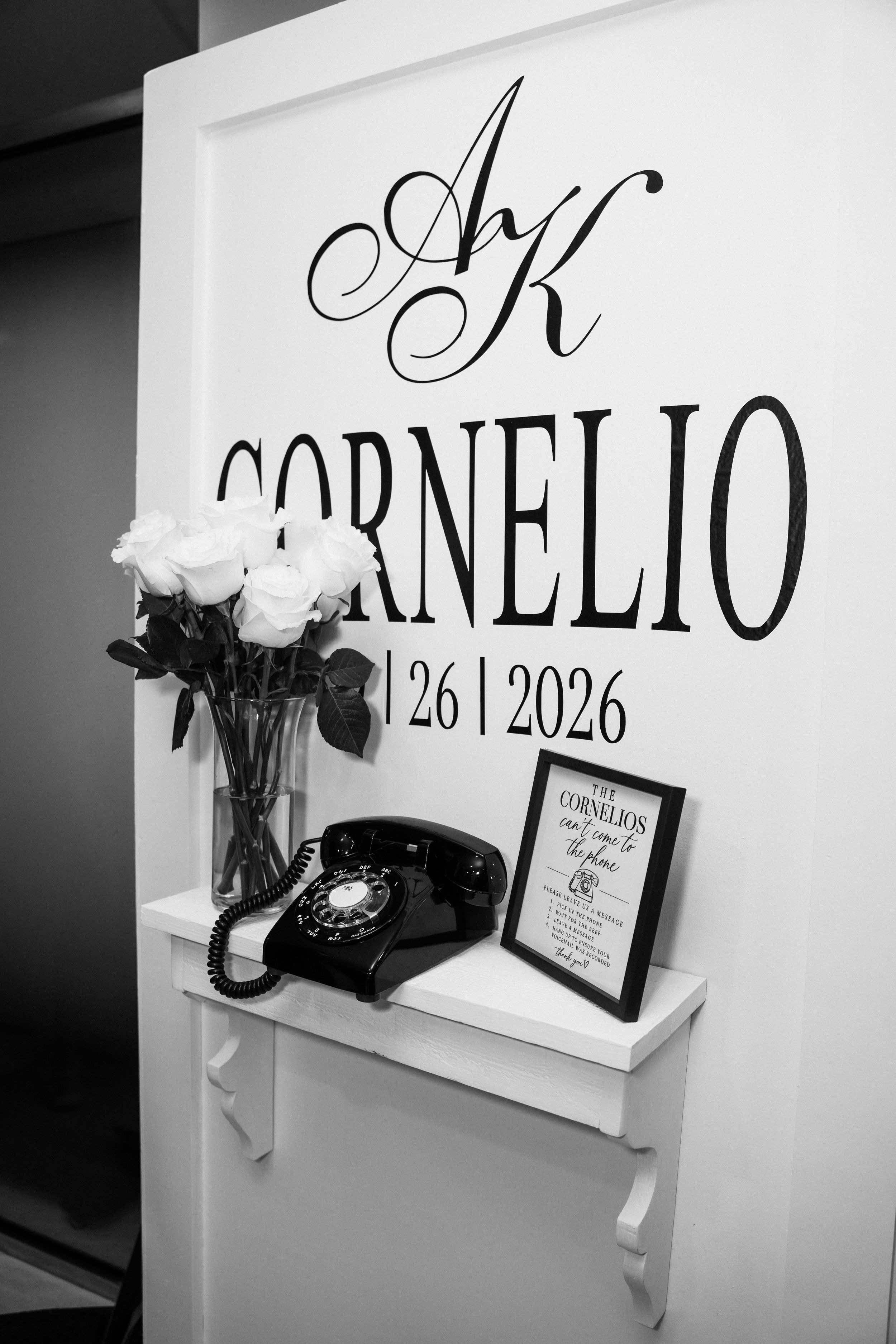 Black and white wedding monogram sign reading Cornelio with roses and vintage rotary telephone decor.