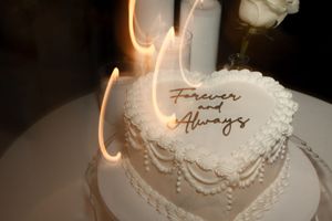 Heart-shaped white wedding cake with Forever and Always topper, decorated with pearl piping and lit sparklers.