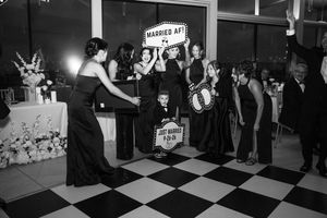 Wedding guests celebrate around a light-up married AF sign on black and white checkered dance floor.
