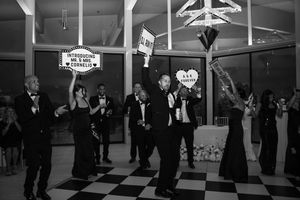 Guests celebrate at a wedding reception on a checkered floor, holding signs introducing Mr. and Mrs. Cornelius.