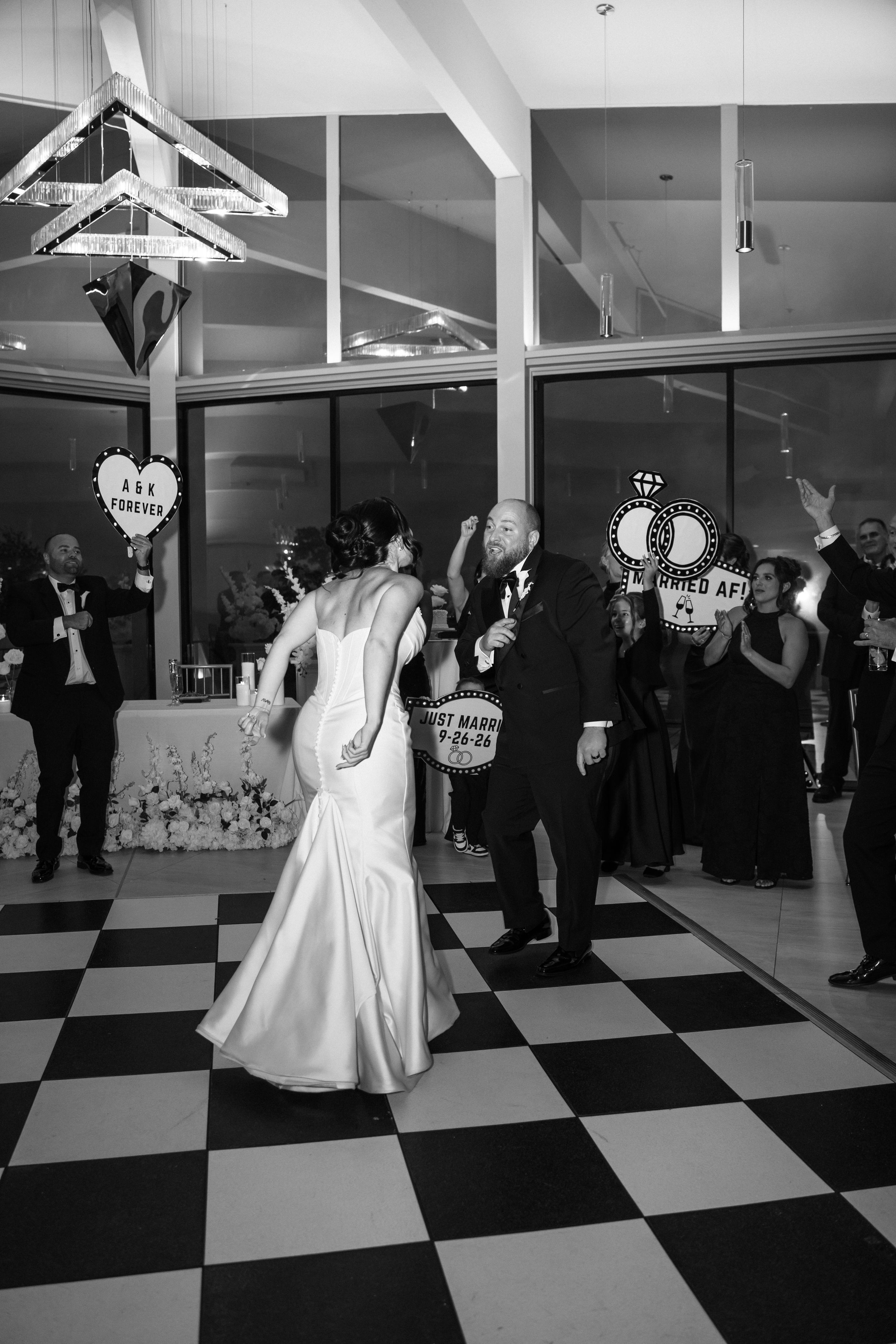 Bride and groom share first dance on black and white checkered dance floor at wedding reception.