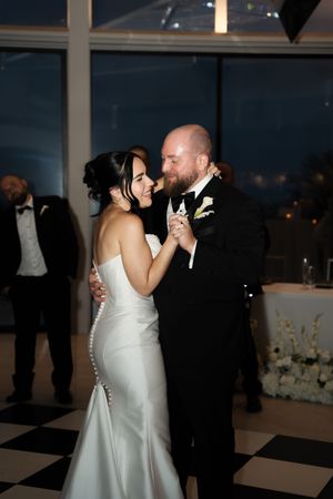 Bride and groom share their first dance on a black and white checkered floor at an elegant wedding reception.