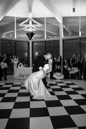 Groom dips bride in romantic first dance moment on classic checkered floor at wedding reception.