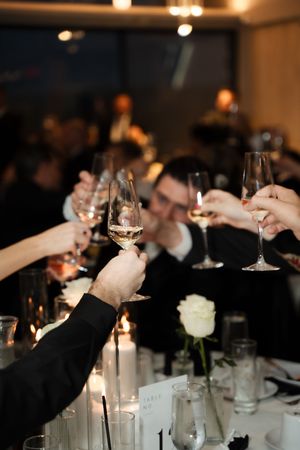 Wedding guests raise champagne glasses in celebratory toast at candlelit reception dinner table.