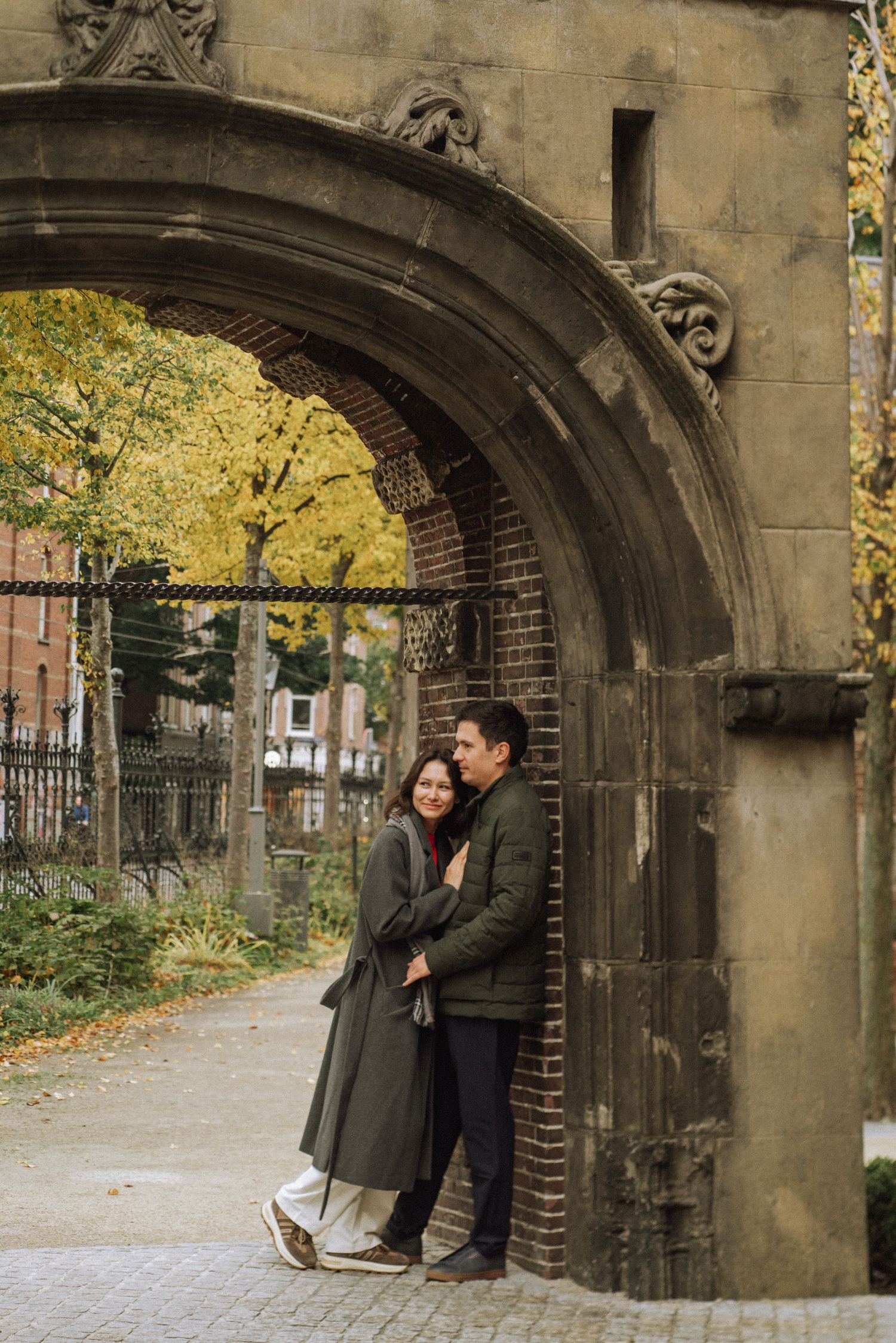 Couple embracing beneath a weathered stone archway with brick walls, Rijksmuseum gardens, Amsterdam.