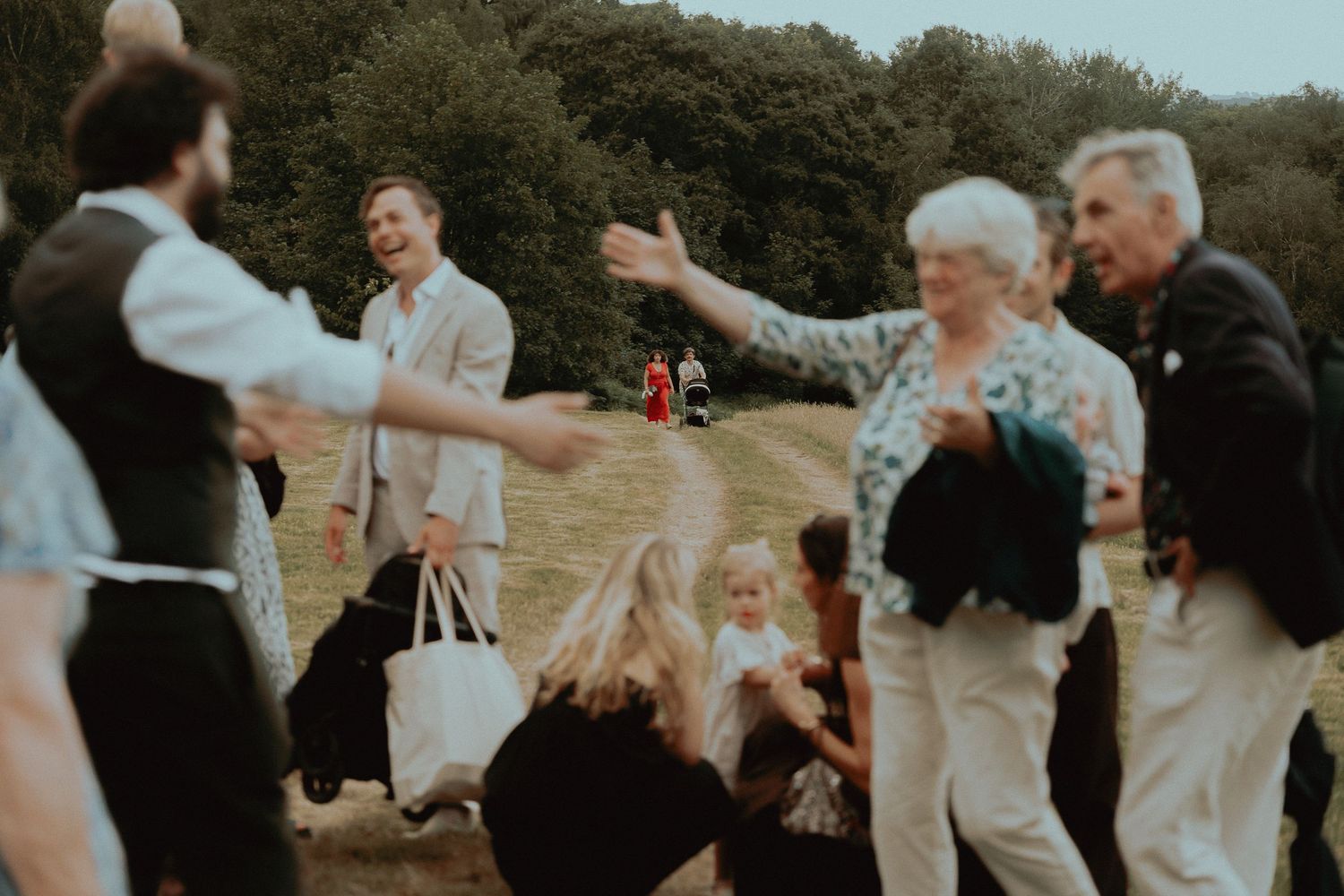 Guests dancing and celebrating outdoors at a wedding reception on a green hillside.