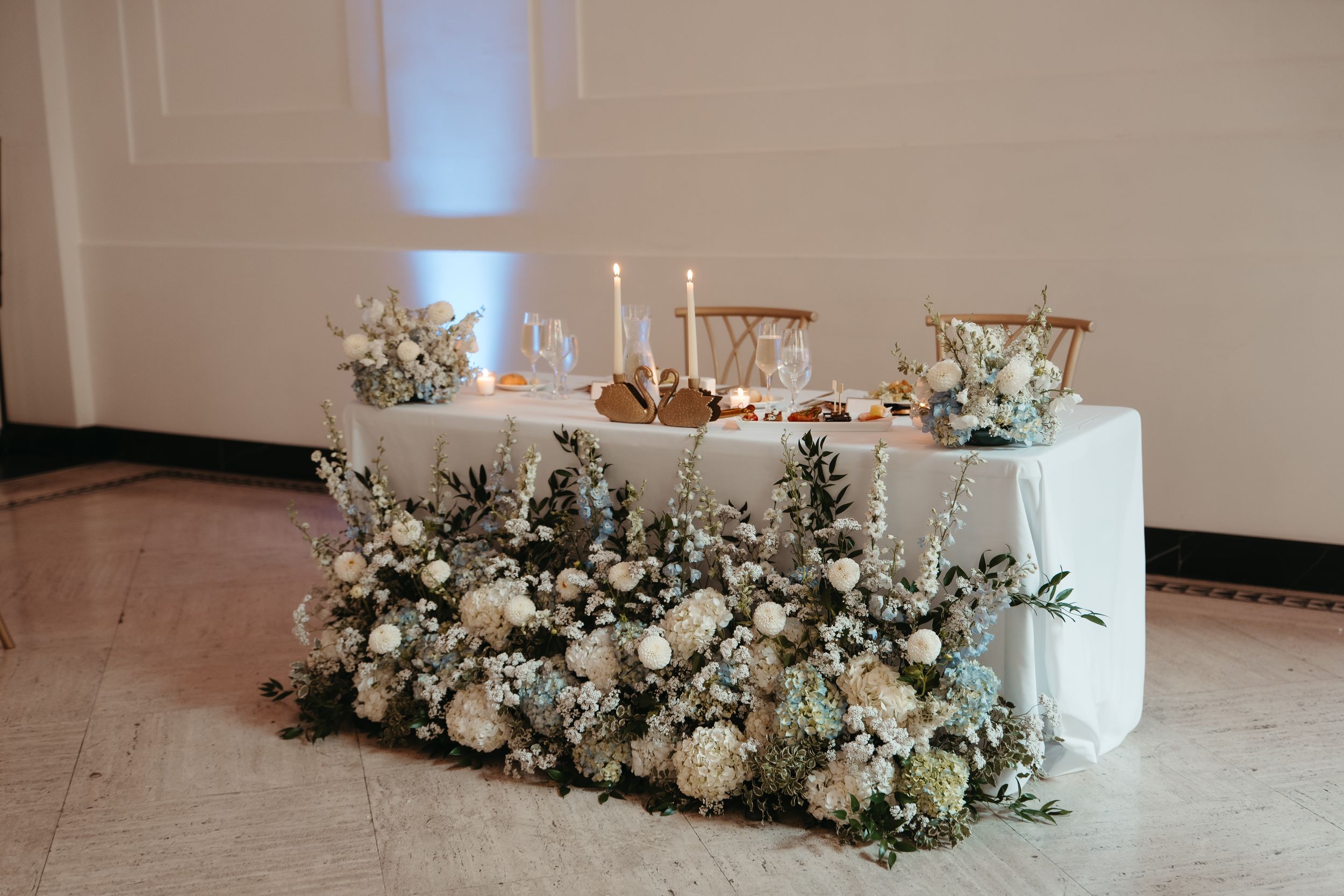 Elegant wedding sweetheart table adorned with white floral arrangements, candles, and a lush floor-level flower display.