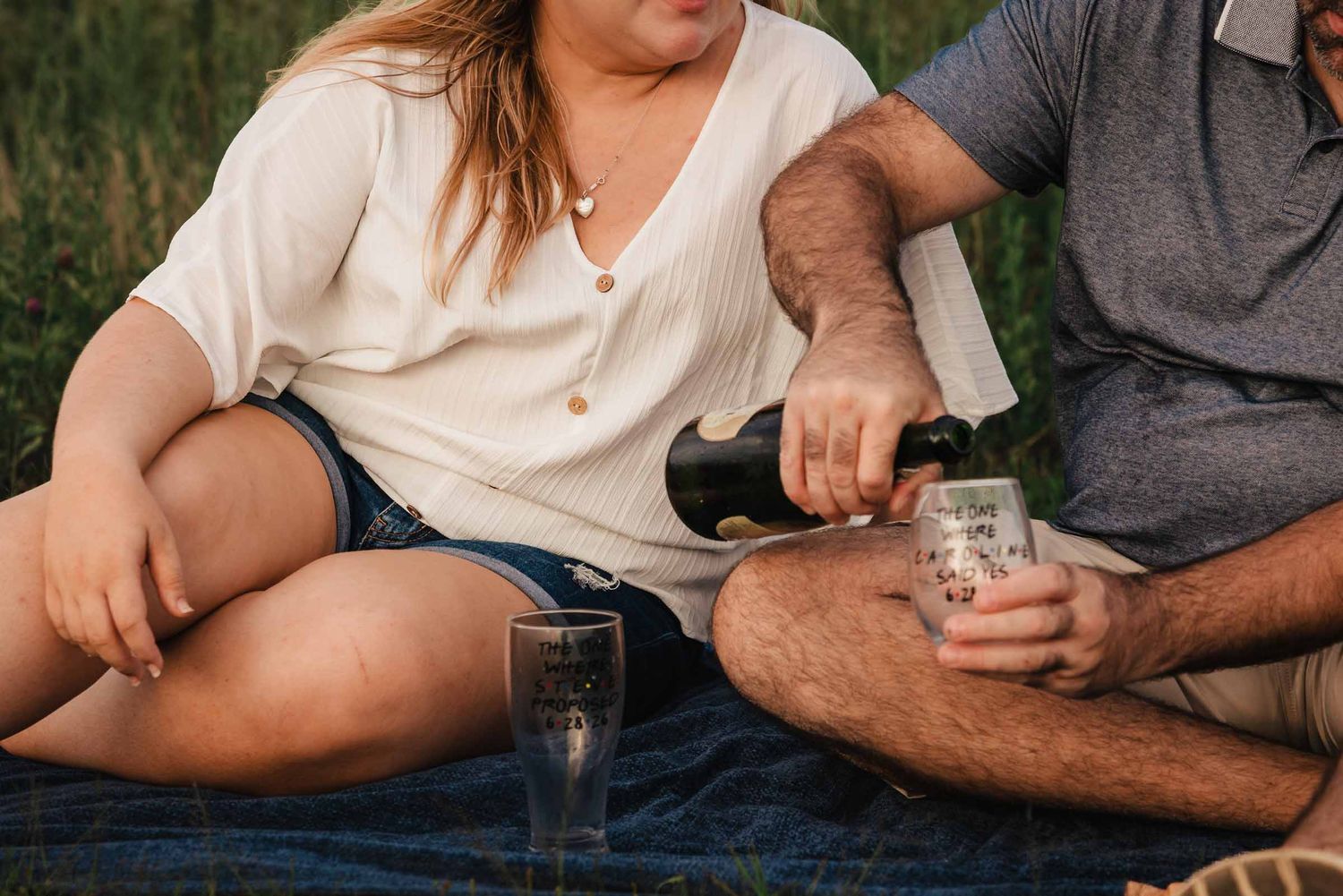 Close-up of champagne being poured into personalized glasses reading wedding date, during a beach picnic.