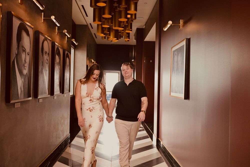 Couple holding hands walking through an elegant hallway with portrait artwork.