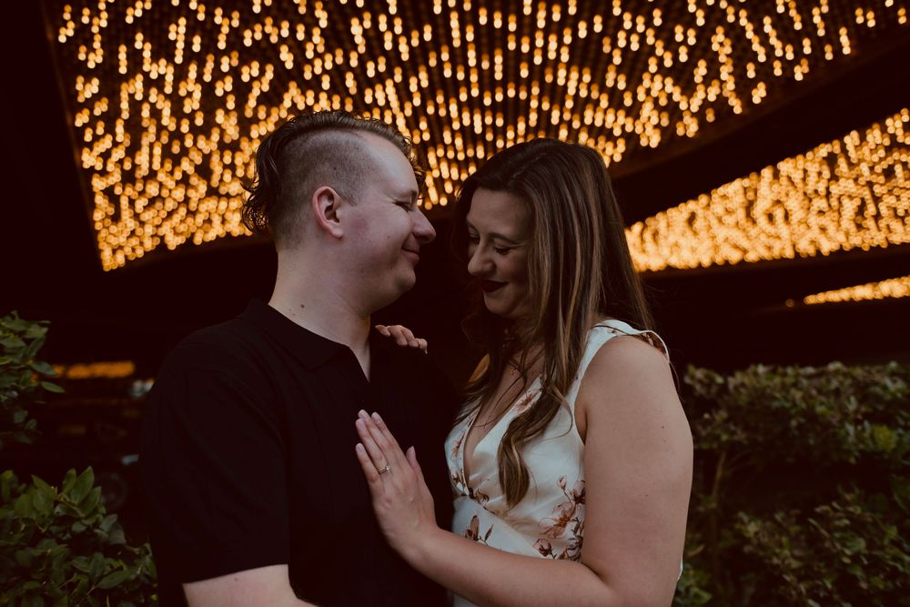 Couple sharing a romantic moment outdoors with warm glowing lights in the background at night.