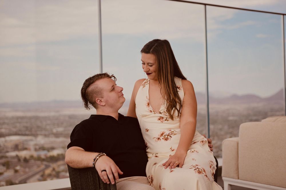 Couple sharing a romantic moment indoors with panoramic mountain and city views through floor-to-ceiling windows.