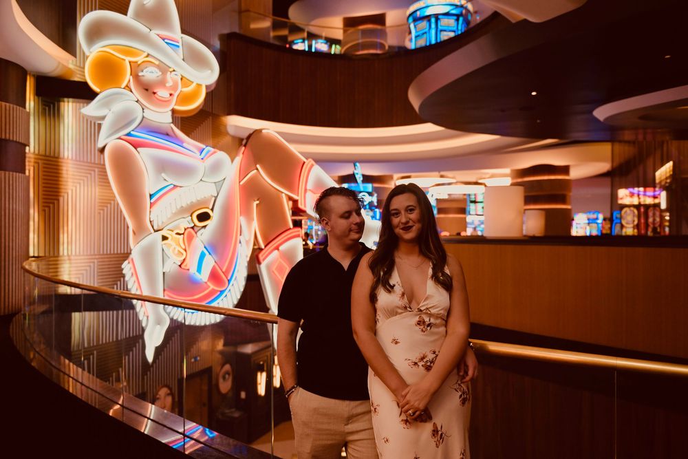 Couple posing together inside a casino near a glowing neon cowgirl sign in Las Vegas.