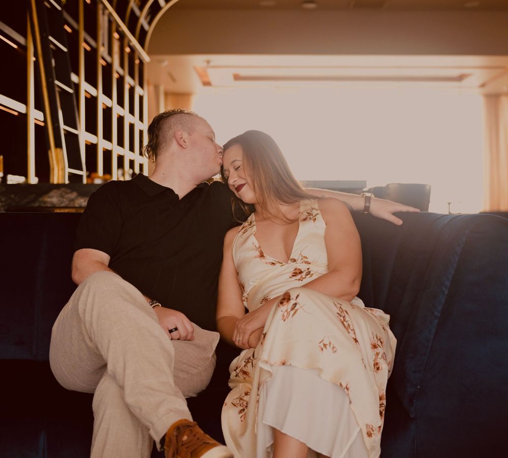 Couple laughing and sharing a romantic moment on a couch in warm golden light.