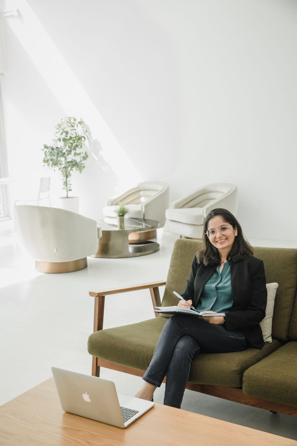 Woman works on laptop while relaxing on olive green couch in minimalist room.