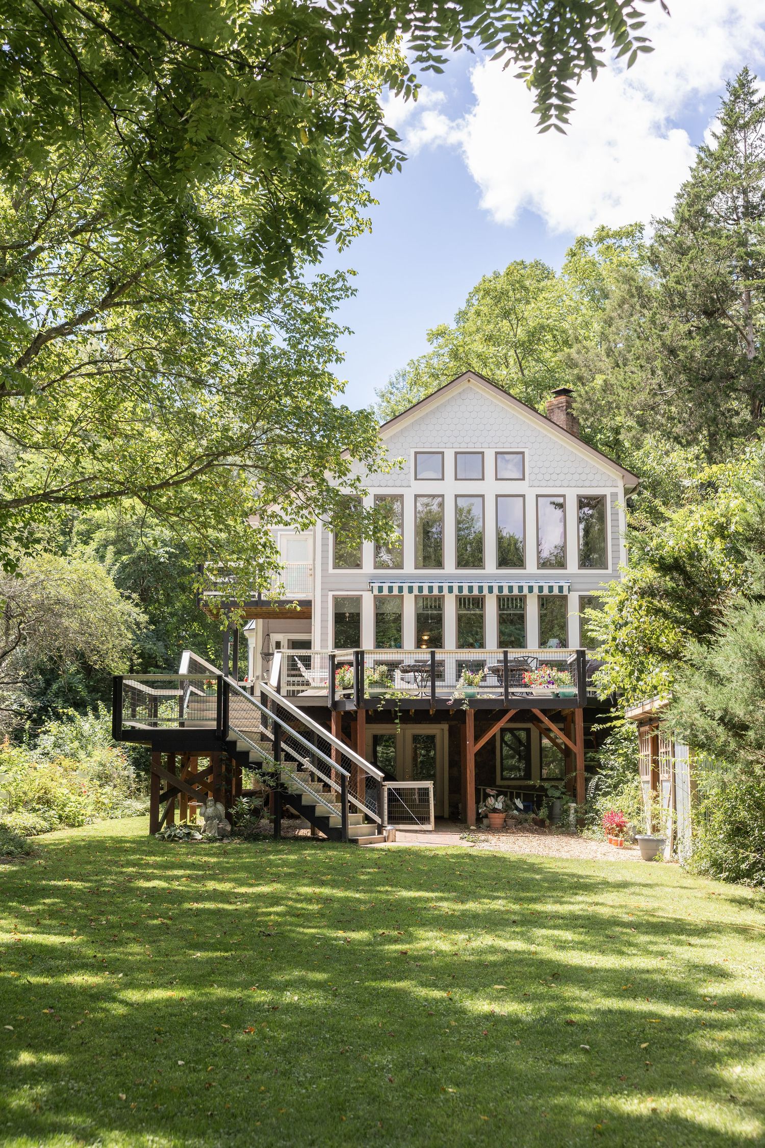 Charming bed and breakfast with lush gardens, pink flowering trees, and a welcoming deck with white railings.