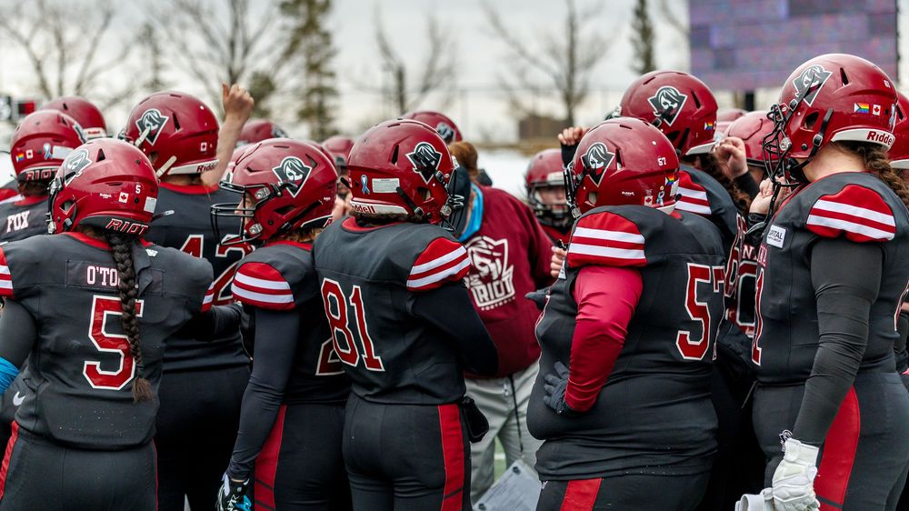 Regina Riot football team huddles together on the field during a game.