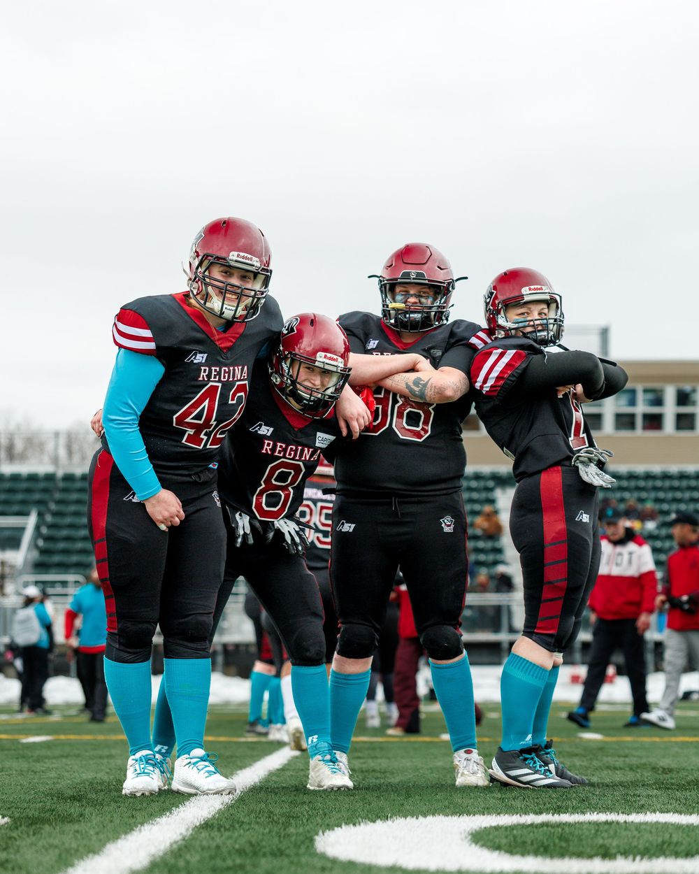 Four Regina Riot football players pose together on the field before a game.