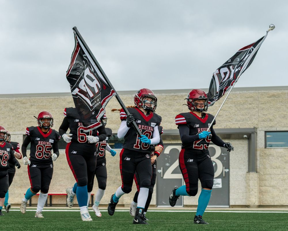 Regina Riot football players run onto the field carrying team flags before a game.