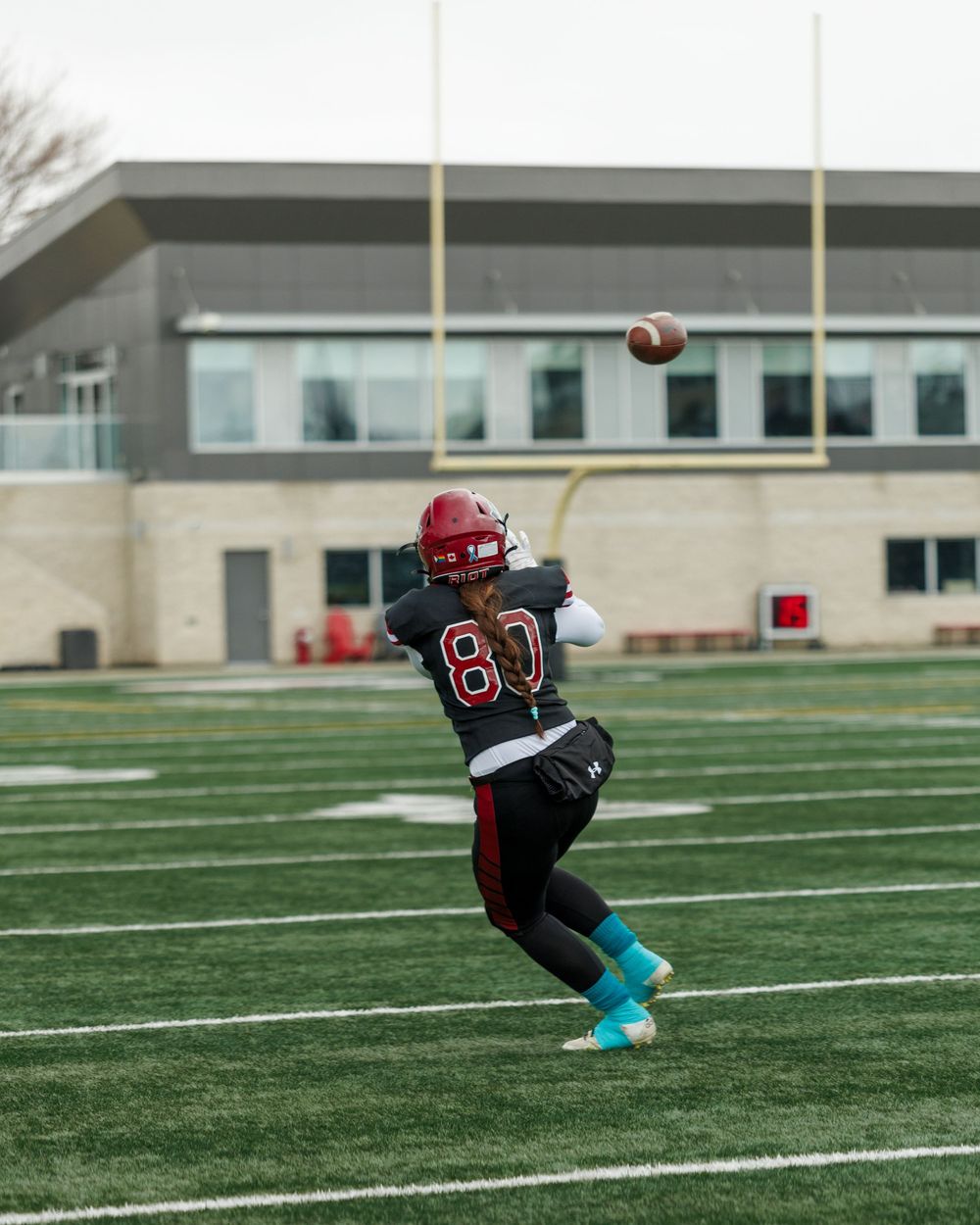 Football player number 80 throwing a pass on an outdoor turf field during practice.
