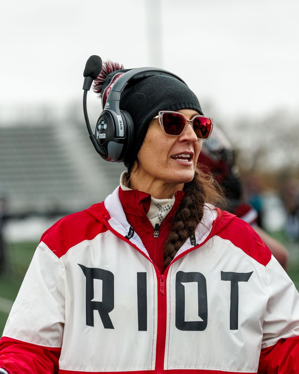 Regina Riot female football coach wearing headset and RIOT jacket on sideline.