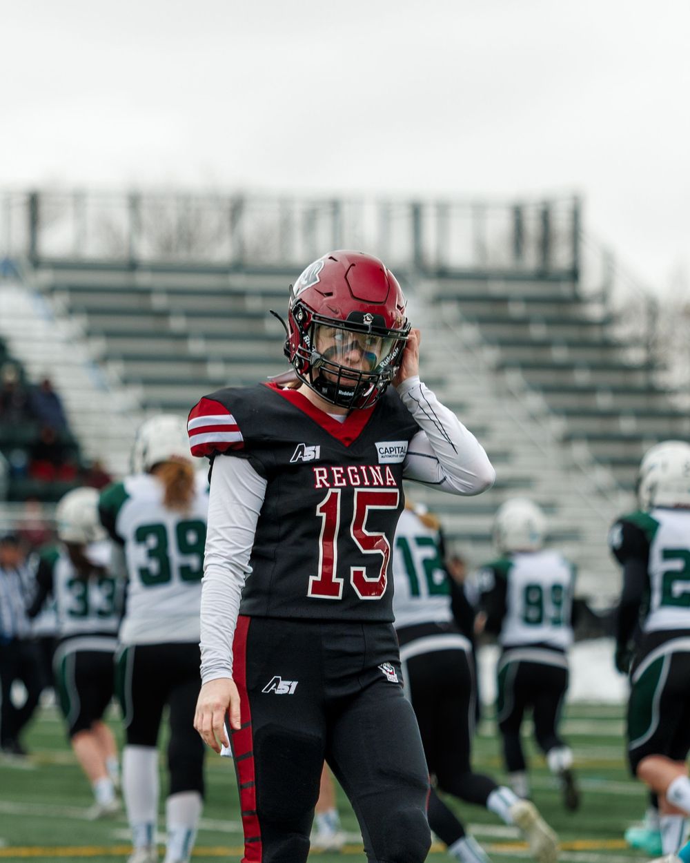 Regina Riot player #15 adjusts helmet on the sideline during a football game.