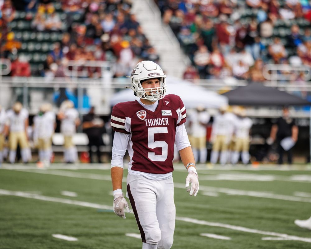 Thunder football player number 5 in maroon jersey walks across the field during a football game.
