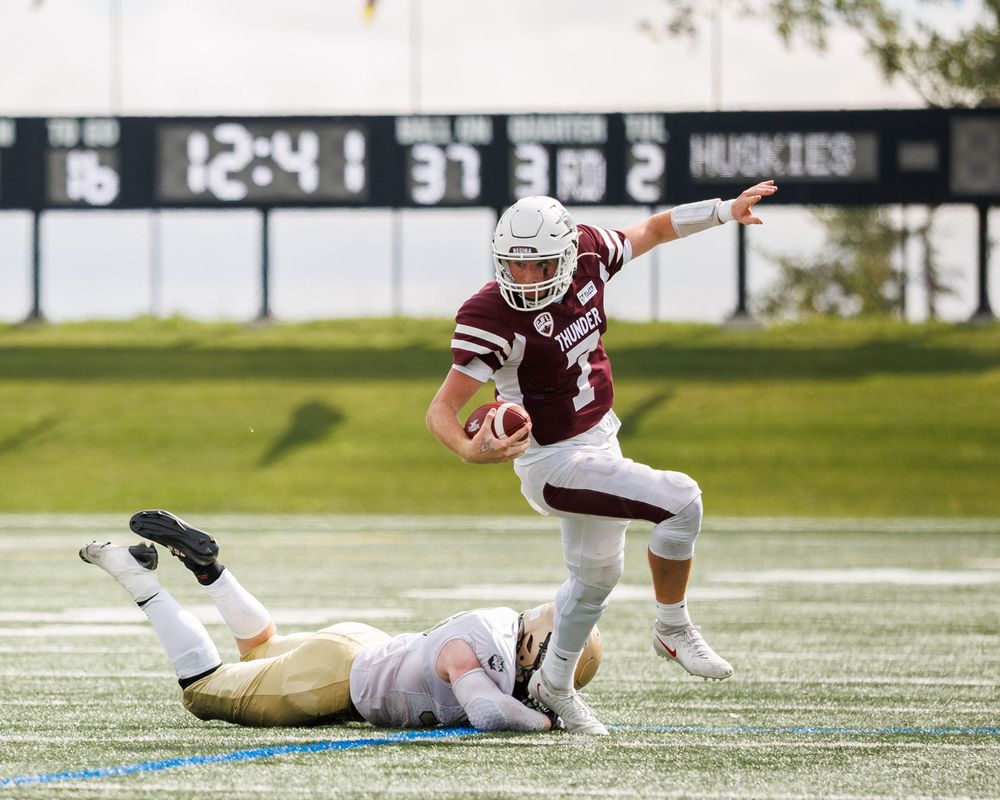 Thunder quarterback evades a diving tackle while running with the football during a competitive game.