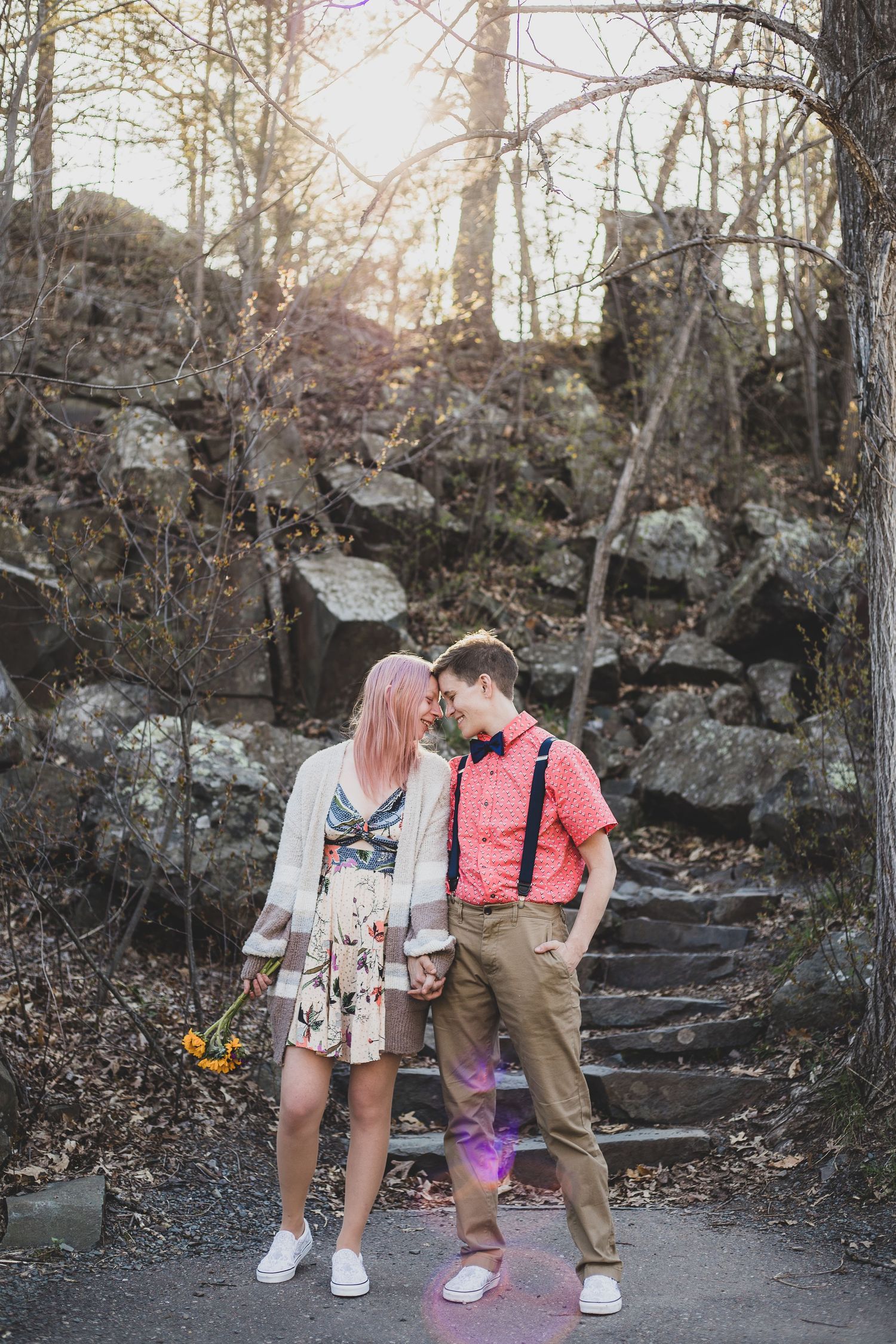 Intimate outdoor photoshoot featuring a couple in vintage-inspired outfits against a rocky forest backdrop.