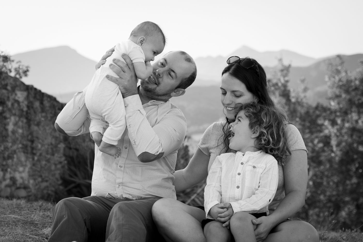 Famille en noir et blanc : un père soulève son bébé, la mère enlace son enfant qui rit, Ardèche