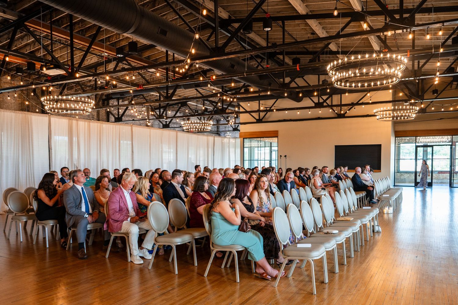 Guests seated in rows of chairs at an elegant indoor wedding ceremony venue with chandelier lighting.