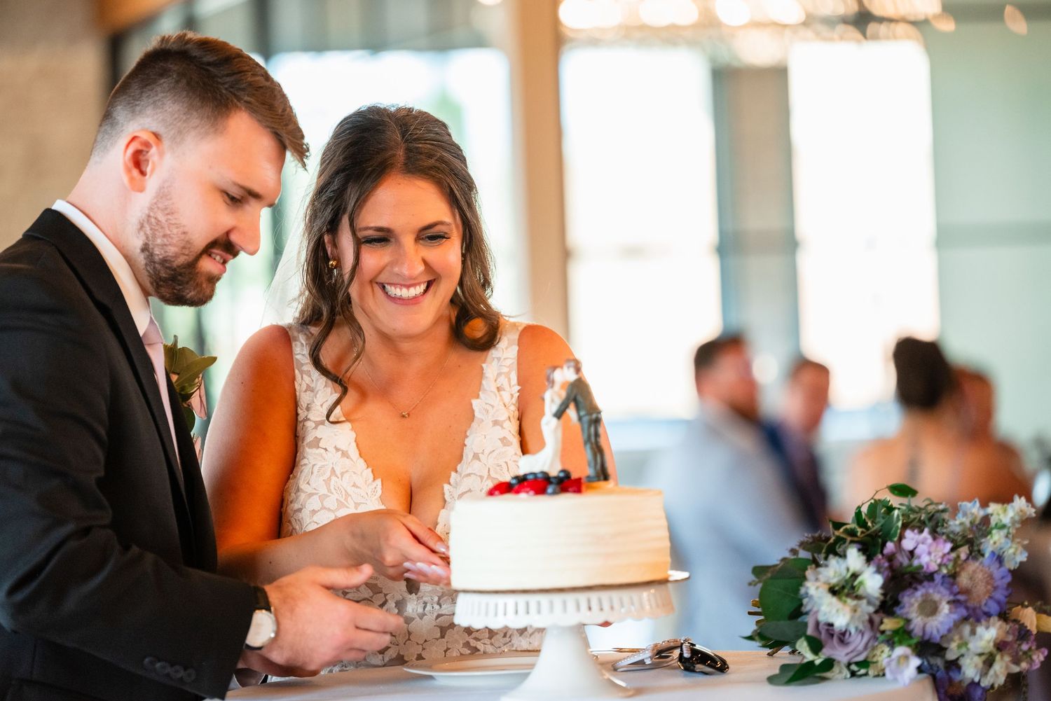 Bride and groom smiling while cutting their white wedding cake together at their wedding reception.