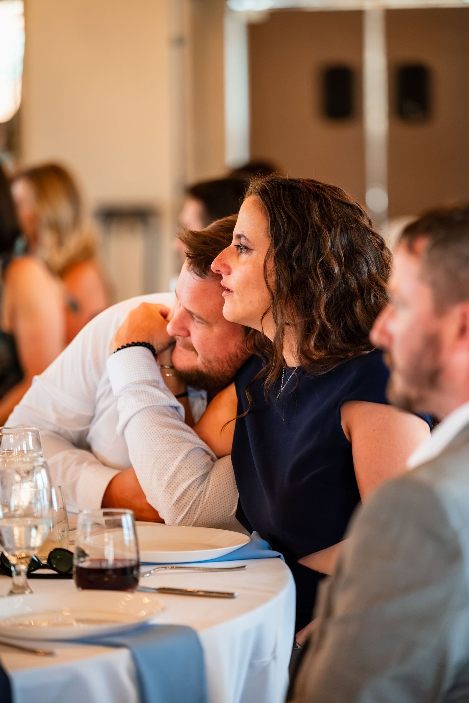Couple sitting closely together at a formal dinner event, woman in navy dress leaning affectionately on man.
