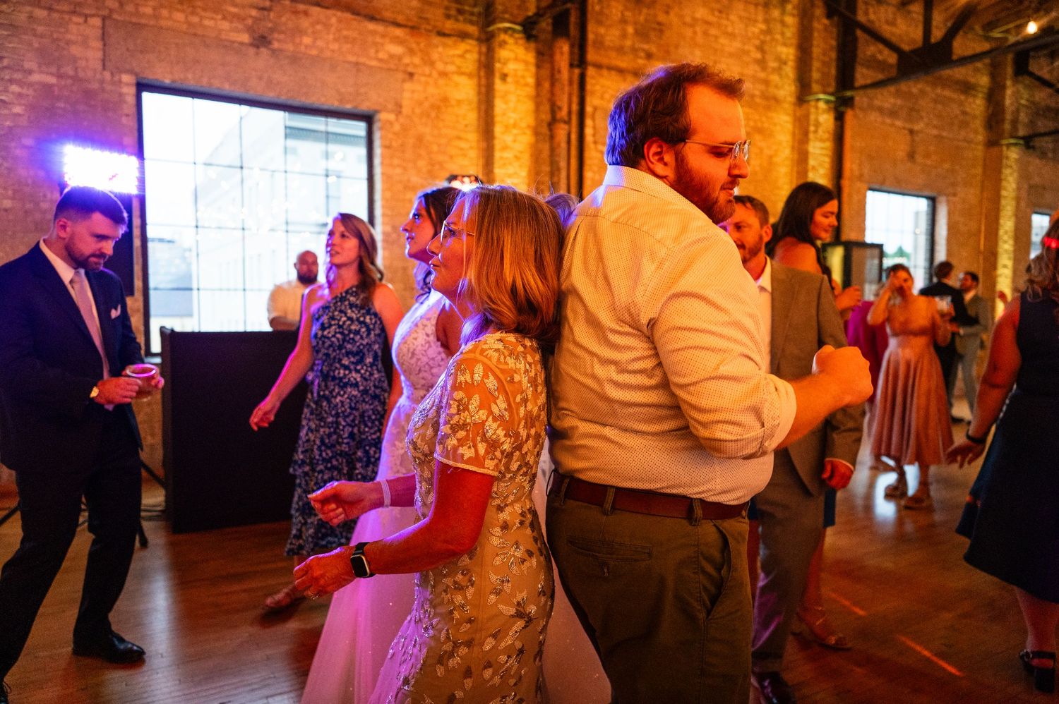 Wedding guests dance and celebrate together in a warmly lit rustic brick reception hall during the evening reception.