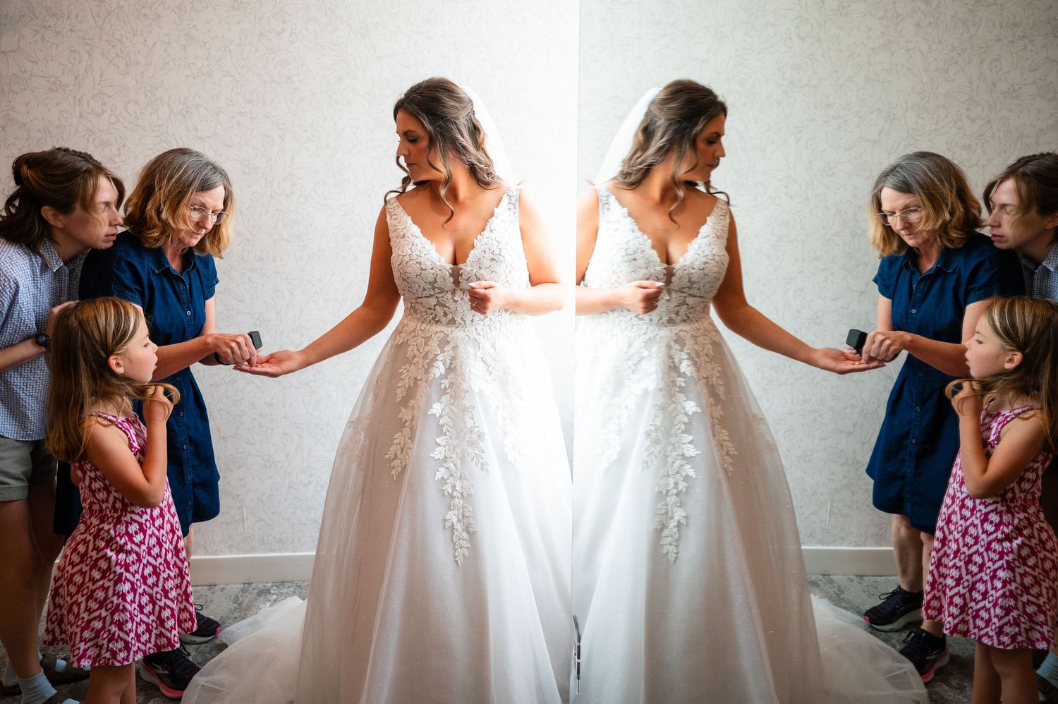 Bride in lace ballgown wedding dress assisted by bridesmaids and flower girl in bright room.