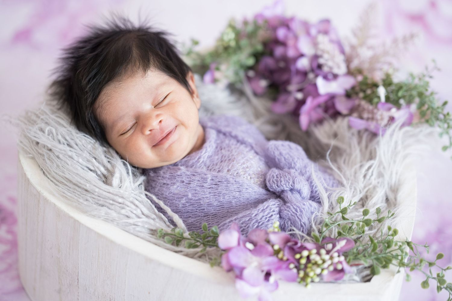 Dreamy newborn portrait with purple flowers and soft lighting creating ethereal atmosphere.