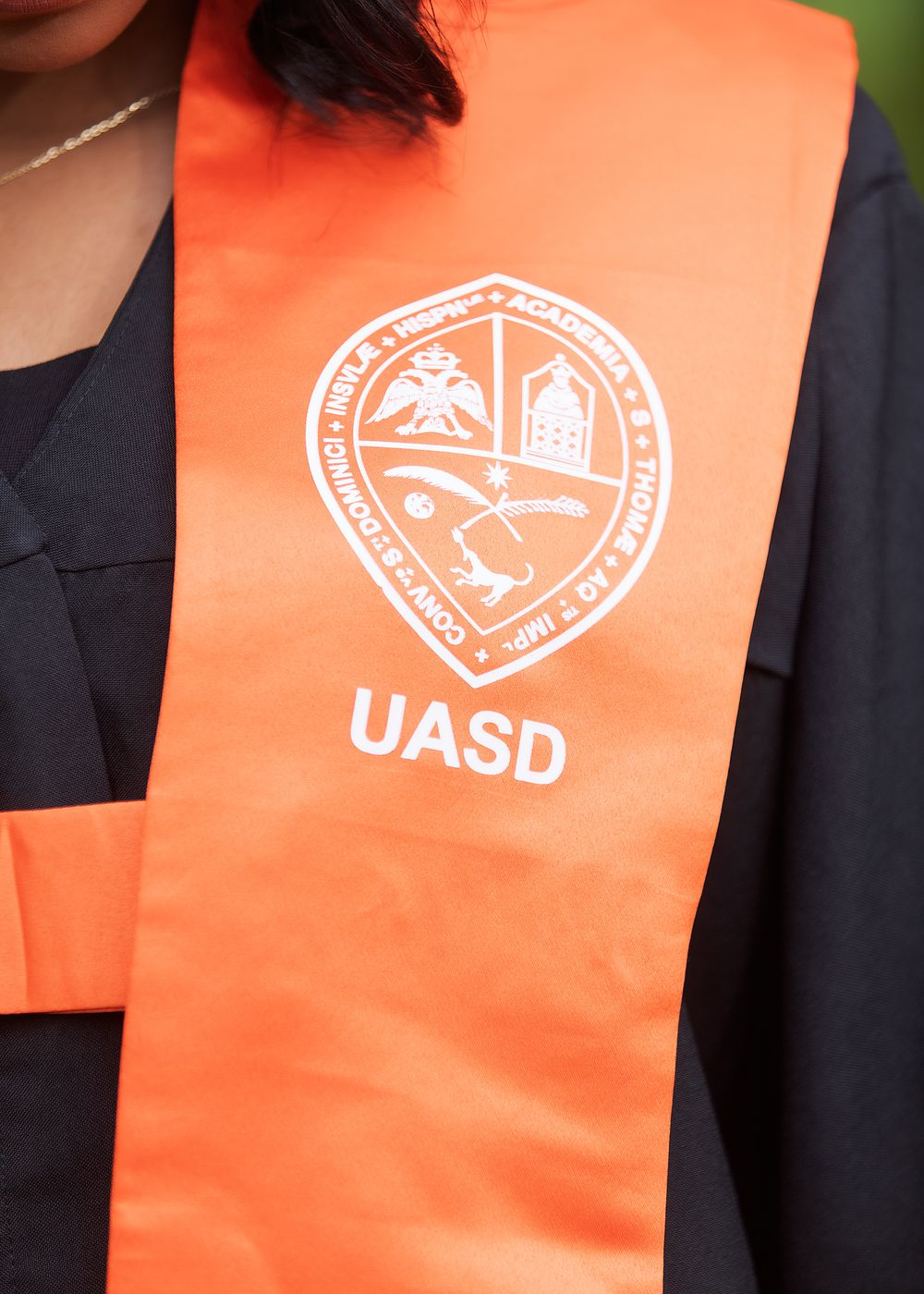 Graduate wearing an orange UASD university graduation stole with official seal over black gown.