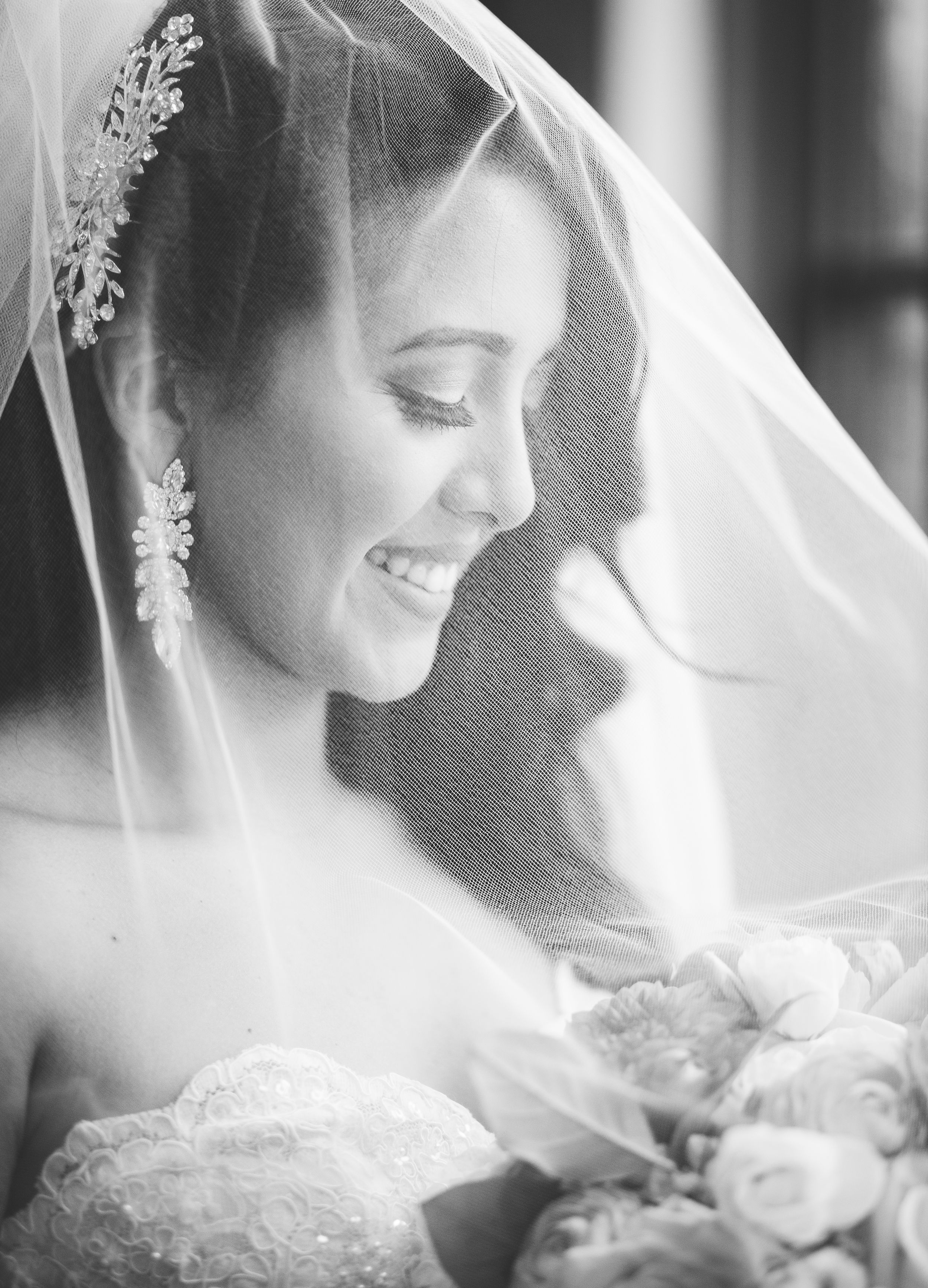 Black and white portrait of smiling bride wearing veil and crystal earrings holding bouquet.