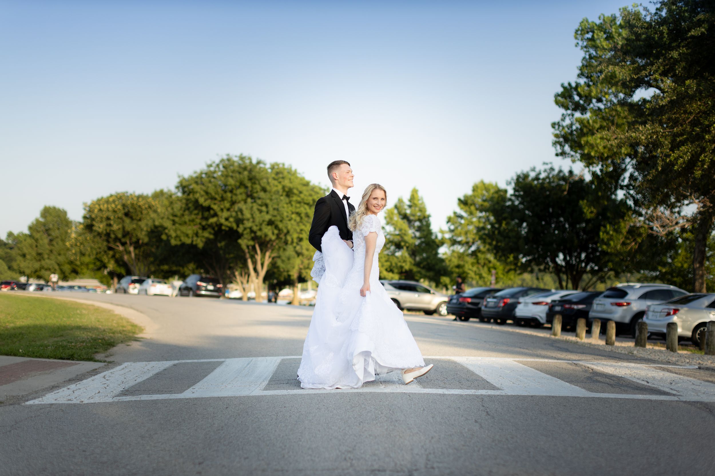 Bride and groom standing together on crosswalk in sunny suburban street after wedding.
