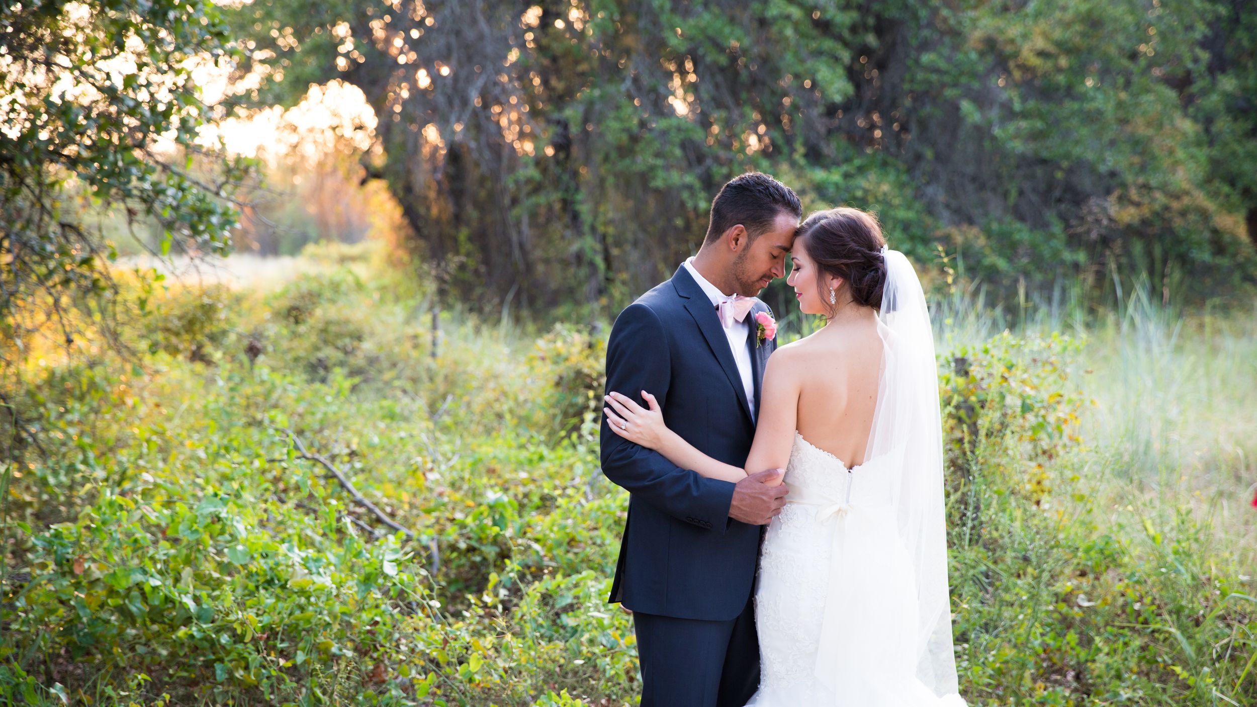 Bride and groom share romantic moment in lush green meadow during golden hour outdoor wedding.