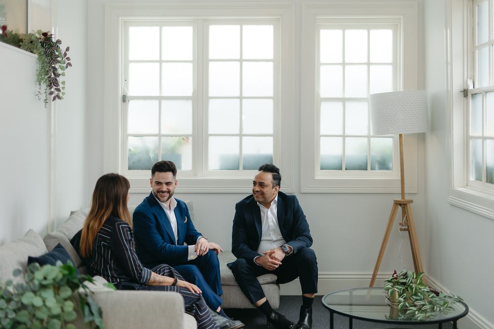 Three professionals engage in a friendly meeting in a bright, modern living room setting.